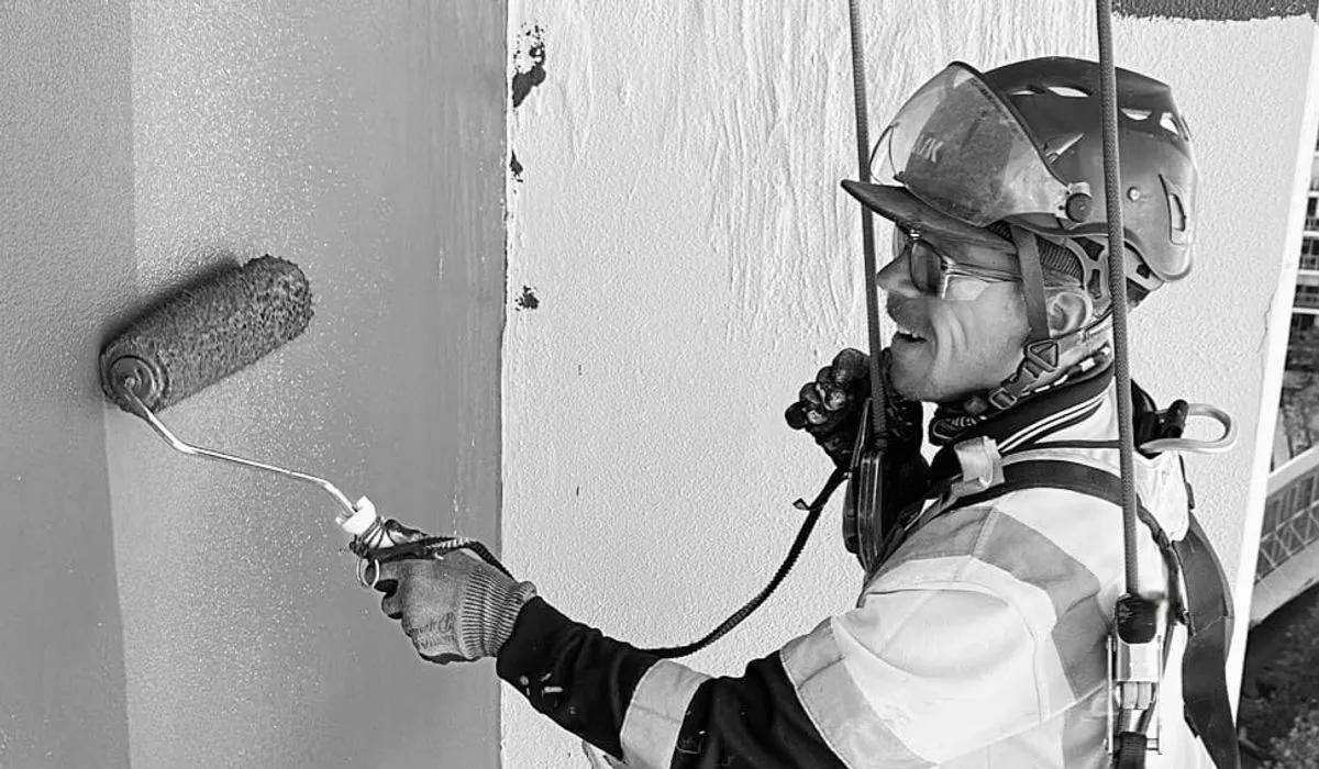 Alpine-Tech 360 rope access technician painting a building wall with a roller while suspended on ropes