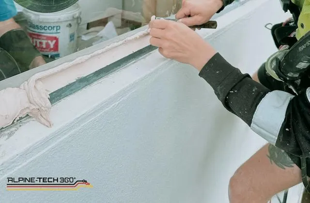 Rope access glazier bedding putty into a window frame during high-rise glass replacement in Auckland